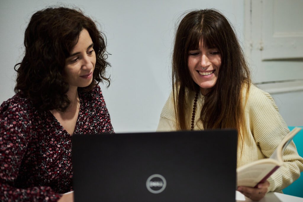 Cristina y Montse trabajando con un libro y un portátil